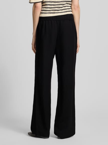Frauenmodel trägt Leinenhose mit elastischem Bund Modell 'Roma' von STEHMANN, schwarze Wide-Leg-Pants aus Reines Leinen, Ganzkörperansicht Rückansicht. Bundweite bei Größe 36: 39 cm, Innenbeinlänge bei Größe 36: 81 cm.