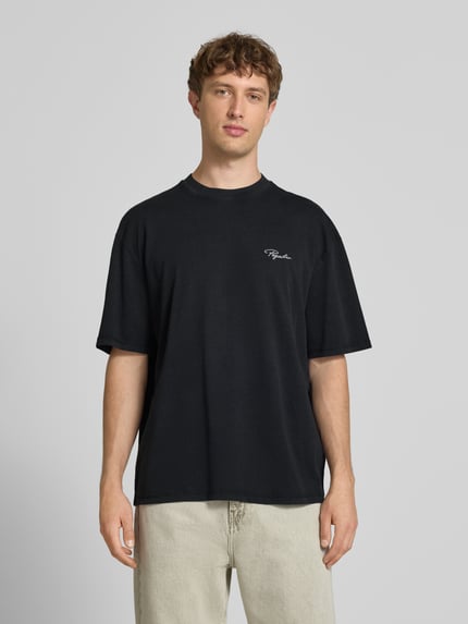 Männermodel trägt Oversized T-Shirt mit Label-Stitching von Pegador, schwarze Reine Baumwolle, Rundhalsausschnitt, Rückenlänge 70 cm, Ganzkörperansicht von vorne.
