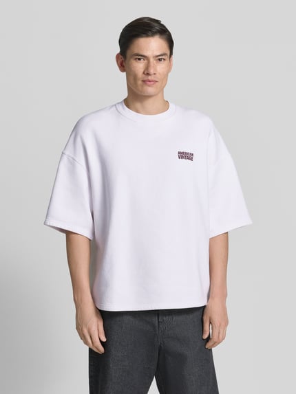Männermodel trägt T-Shirt mit Logo Modell 'PLIZZY' von American Vintage, reine Baumwolle, relaxed Fit, weiß, Nahaufnahme Oberkörper.