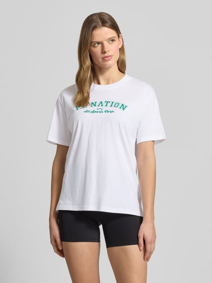 Frauenmodel trägt T-Shirt mit Logo-Print und Rundhalsausschnitt von P.E Nation aus Reine Baumwolle im Relaxed-Fit, Rückenlänge 64 cm, Ganzkörperansicht von vorne.