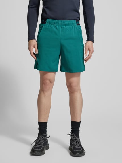 Männermodel trägt Straight Fit Shorts mit Logo-Print Modell 'Vanish' von Under Armour, grün, elastischer Bund, Eingrifftaschen, Ganzkörperansicht von vorne.