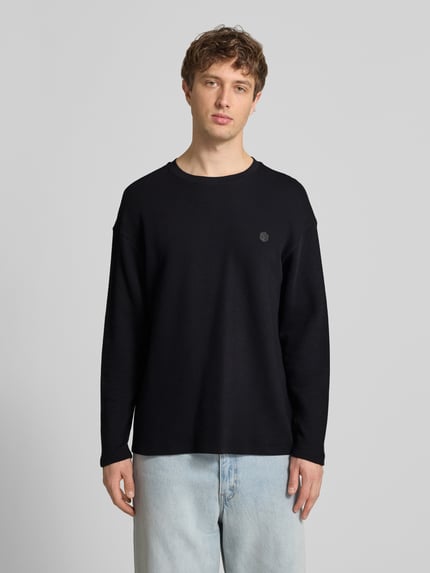 Männermodel trägt Longsleeve aus Baumwolle Modell 'FILLIP' von Blend, schwarze Farbe, Gerader-Schnitt, Label-Detail, Ganzkörperansicht von vorne. Rückenlänge bei Größe M: 70 cm.