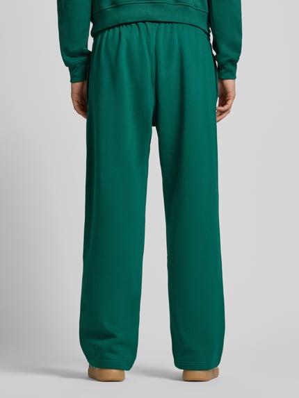Männermodel trägt Wide Fit Sweathose mit elastischem Bund von adidas Originals aus Mieszanka bawełny, krój wide fit, wpuszczane kieszenie, wyhaftowane logo, długość wewnętrzna nogawki w rozmiarze M: 80 cm, kolor zielony, gładka tekstura. Ganzkörperansicht Rückansicht.