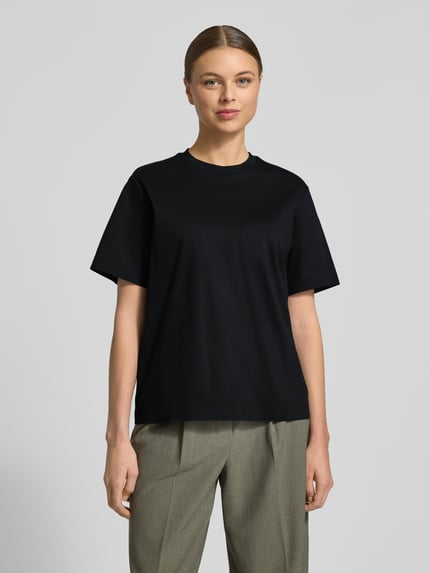 Kobiece modelka nosi Relaxed Fit T-Shirt aus reiner Baumwolle Modell 'EHARPA' od BOSS, czarny kolor, luźny krój, cienka bawełniana faktura, okrągły dekolt, krótkie rękawy, minimalny branding, widok całej sylwetki z przodu.