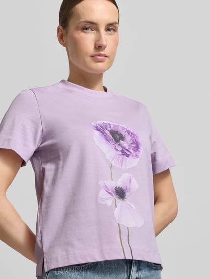 Frauenmodel trägt T-Shirt mit Motiv-Print Modell 'FIORE' von Stefanel in Flieder mit Blumenmuster, Baumwolle, gerader Schnitt, Nahaufnahme Oberkörper.