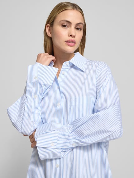 Vrouwenmodel draagt Hemdbluse mit Knopfleiste Modell 'Benice' van JOOP!, blauw-wit gestreept, losse pasvorm, borst detailopname, Lyocell-katoen-mix met stretch.