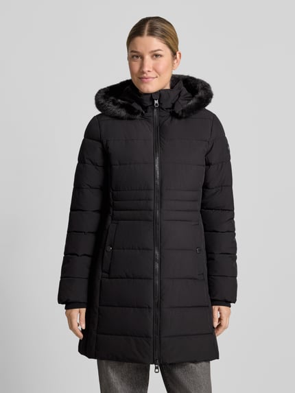 Frauenmodel trägt Jacke mit abnehmbarer Kapuze Modell 'ECLIPSE' von NAUTGÅRD in Schwarz, sichtbare Druckknopftaschen, dezente Steppstruktur, Zweiwege-Reißverschluss, Label-Patch, gestrickte Ärmelabschlüsse, gerader Schnitt, Ganzkörperansicht von vorne. Rückenlänge bei Größe S: 79 cm, Schulterbreite: 38 cm, Brustweite: 48 cm, Ärmellänge: 62 cm.