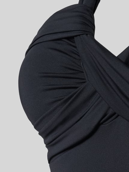 Vrouwenmodel draagt 'Body mit Neckholder' van Seafolly in zwart, stretchmateriaal met plooien, close-up buste, detailopname.