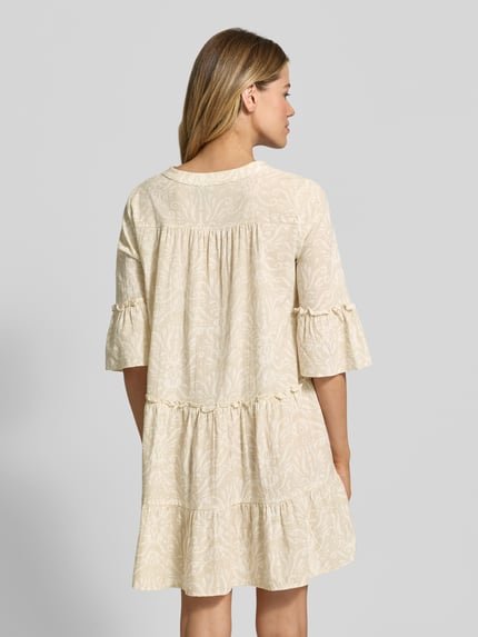Männermodel trägt Ausgestelltes Blusenkleid aus reiner Baumwolle Modell 'DICTHE' von Vero Moda, kremowe Allover-Muster, trompetenförmige rękawy, długość mini, tkanina bawełniana, marszczenia, Ganzkörperansicht Rückansicht.