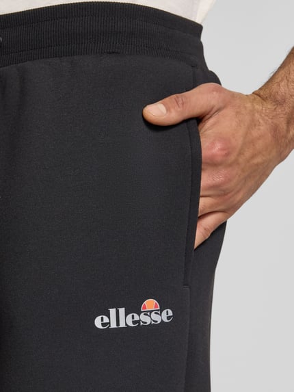 Mannenmodel draagt Sweatpants met Logo model 'SIRTORI' van Ellesse, zwart, zachte textuur, regular fit, close-up taille en zak, detailopname.