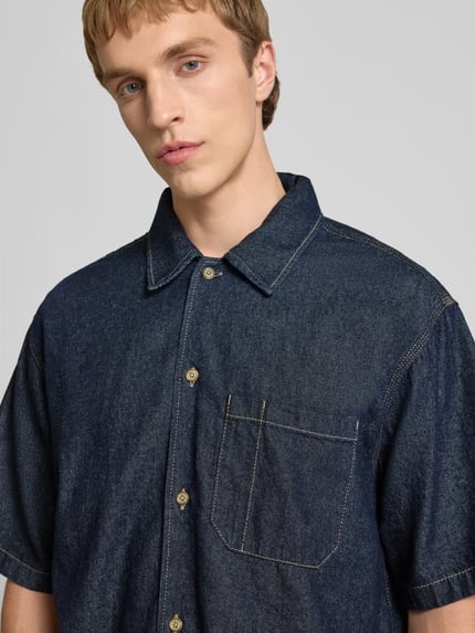 Männermodel trägt Relaxed Fit Jeanshemd mit Brusttasche von Dickies in dunklem Blau, Reine Baumwolle, Nahaufnahme Oberkörper.