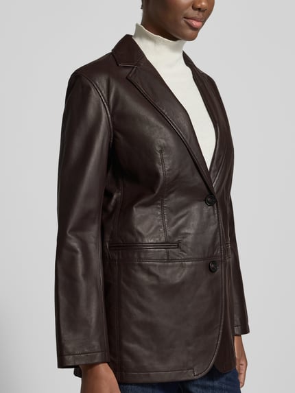 Frauenmodel trägt Regular Fit Longline Lederjacke aus Lammnappa von Marc O'Polo in dunkelbrauner Lederoptik mit Struktur, 2-Knopf-Verschluss, Reverskragen, Paspeltaschen, Label-Detail und Teilungsnähten, unifarben, Nahaufnahme Oberkörper.