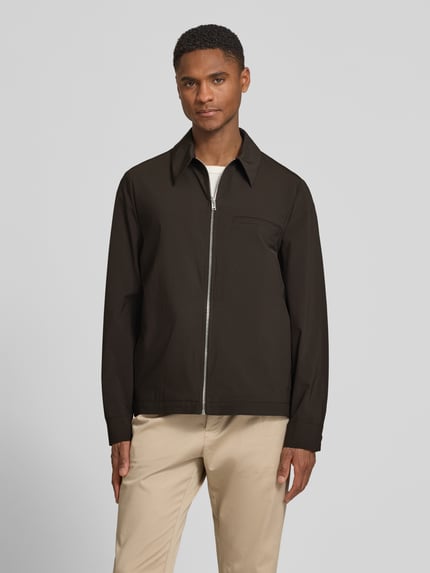 Männermodel trägt Jacke mit Kentkragen und Reißverschluss Modell 'JOTTAR' von Drykorn in Regular-Fit, Ganzkörperansicht von vorne, Rückenlänge bei Größe M: 73 cm, Schulterbreite: 40 cm, Brustweite: 48 cm, Ärmellänge: 65 cm, Beige Hose, dunkler Stoff, glatte Textur.