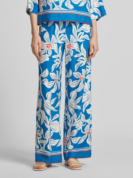 Vrouwenmodel draagt stoffen broek van viscose model 'Rylie' van GUIDO MARIA KRETSCHMER WOMAN, relaxed fit, all-over look, elastische band, blauw met witte bloemen, bandwijdte maat 36: 36 cm, binnenbeenlengte maat 36: 77 cm. Nahaufnahme onderlichaam.