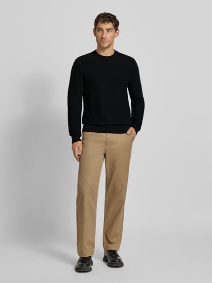 Männermodel trägt Regular Fit Strickpullover aus reiner Baumwolle Modell 'IMBERTO' von BOSS in Schwarz, Strukturmuster, Ganzkörperansicht von vorne.