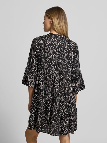 Frauenmodel trägt Ausgestelltes Blusenkleid aus reiner Viskose Modell 'EASY JOY' von Vero Moda, Optik:Allover-Muster, 3/4-Arm, Trompetenärmel, Mini-Länge, Henley-Ausschnitt, Raffung, Material: reine Viskose, Ganzkörperansicht Rückansicht.