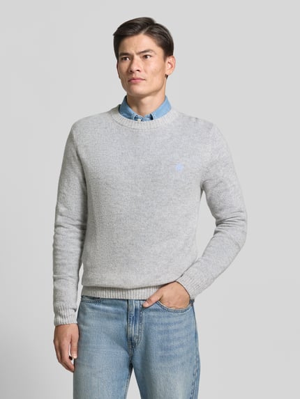 Männermodel trägt Slim Fit Strickpullover aus reiner Wolle mit Label-Stitching von MCNEAL in Hellgrau, gerippte Abschlüsse, Nahaufnahme Oberkörper.