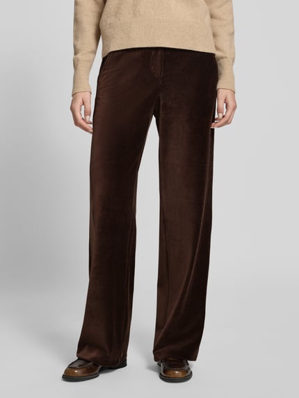 Frauenmodel trägt Regular Fit Cordhose mit Bundfalten Modell 'MAINE' von BRAX in Dunkelbraun, unifarben, strukturierte Cord-Oberfläche, seitliche Eingrifftaschen, Gesäßtaschen, Gürtelschlaufen, Knopf und verdeckter Reißverschluss, Ganzkörperansicht von vorne.