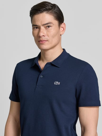 Männermodel trägt Regular Fit Poloshirt aus Baumwoll-Mix von Lacoste in uni navy, Polokragen, kurzarm, Logo-Patch, Nahaufnahme Oberkörper.