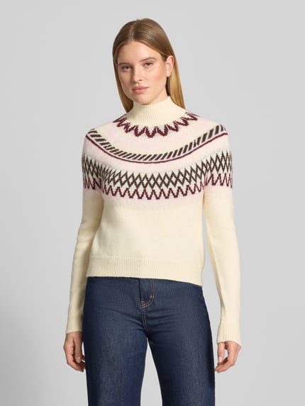 Frauenmodel trägt Pullover mit Jacquardpasse Modell 'VMMAPLE' von VERO MODA in mehrfarbiger Strickoptik mit geometrischen Rautenmustern, hochgeschlossenem Mock Neck, langen Ärmeln und gerippten Abschlüssen, Ganzkörperansicht von vorne.