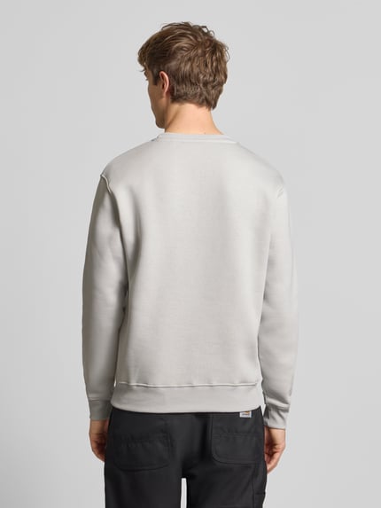 Männermodel trägt Regular Fit Sweatshirt aus Baumwoll-Mix mit Label-Detail von Alpha Industries, helle Farbe, elastische Abschlüsse, Ganzkörperansicht Rückansicht.