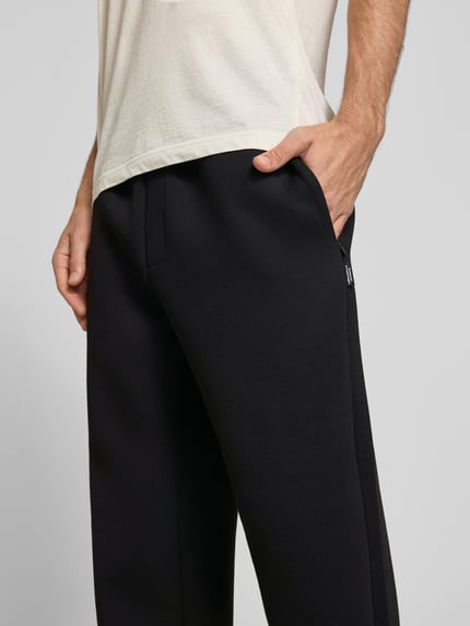 Männermodel trägt Regular Fit Sweatpants aus Material-Mix Modell 'BILL LEGACY' von JACK & JONES in Schwarz, Nahaufnahme Oberschenkel, Herren Sweatpants mit Eingrifftaschen, elastischer Bund mit Tunnelzug, Material-Mix, Innenbeinlänge bei Größe M 77 cm.