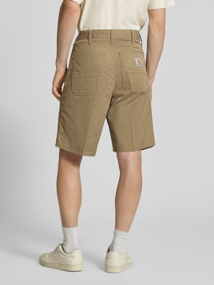 Männermodel trägt Bermudas mit Gesäßtaschen von Carhartt Work In Progress in Beige, Material-Mix mit Baumwoll-Anteil, Regular-Fit, Eingrifftaschen, Bundweite 45 cm, Innenbeinlänge 26 cm, Ganzkörperansicht Rückansicht.