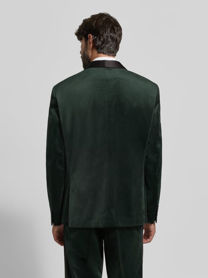 Männermodel trägt Slim Fit Anzug aus Samt von Lindbergh in dunklem Grün, glatte Textur, Ganzkörperansicht Rückansicht. Kontext: Schalkragen, Knopfverschluss, Sakko mit Brust- und Pattentaschen, Einstecktuch, Anzughose mit Haken-, Knopf- und Reißverschluss, Maße bei Größe 50: Rückenlänge 74 cm, Schulterbreite 48 cm, Ärmellänge 67 cm.