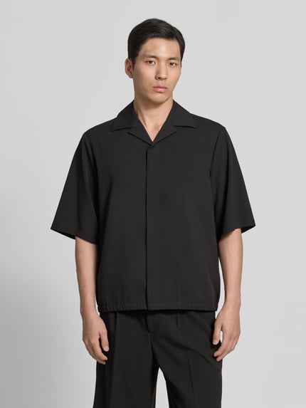 Męski model nosi Relaxed Fit Hemdjacke mit Reverskragen od Lindbergh, czarny materiał z domieszką wiskozy, ukryta listwa guzikowa, długość tyłu w rozmiarze M: 69 cm, szerokość ramion w rozmiarze M: 48 cm, długość rękawa w rozmiarze M: 34 cm, widok całej sylwetki z przodu.