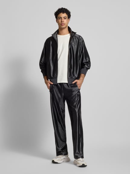Männermodel trägt Trainingshose mit Logo Modell 'FIREBIRD' von adidas Originals in Schwarz, Regular Fit, elastischer Bund, Ganzkörperansicht von vorne.