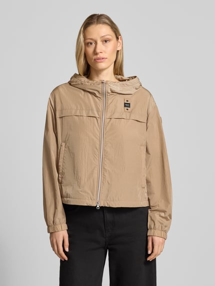 Frauenmodel trägt Trekking Jacke mit Kapuze Modell 'BURRAGE' von Blauer Usa in Beige, zweiwege-Reißverschluss, gerade geschnitten, Label-Patch, seitliche Reißverschlusstaschen, elastische Ärmelabschlüsse, glatte Textur, Ganzkörperansicht von vorne