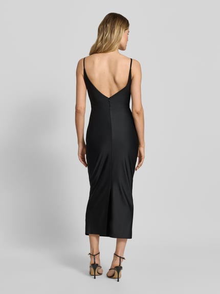 Modelka nosi Cocktailkleid mit Spaghettiträgern und V-Ausschnitt von TROYDEN COLLECTION, czarny satynowy materiał, dopasowany krój slim fit, długość midi, dekolt i plecy w kształcie V, zamek z tyłu, długość tyłu w rozmiarze 36: 125 cm, szerokość w rozmiarze 36: 37 cm, ujęcie całej sylwetki z tyłu.