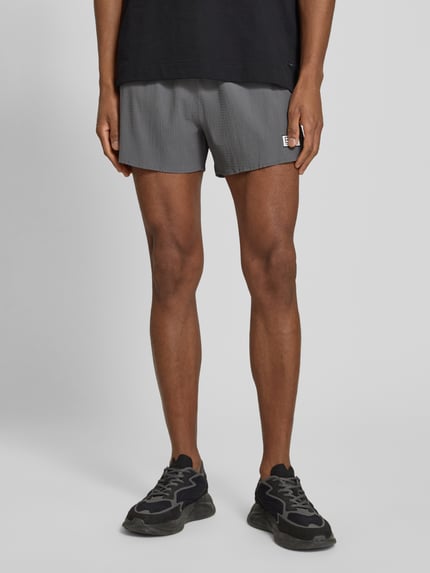 Männermodel trägt Relaxed Fit Shorts mit integriertem Slip von EA7 Emporio Armani, Elastischer-Material-Mix, Strukturmuster, Logo-Patch, Bund, Ganzkörperansicht von vorne.
