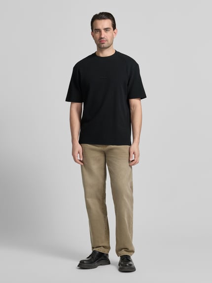 Männermodel trägt Regular Fit T-Shirt aus reiner Baumwolle Modell 'DAFFL' von HUGO in Schwarz, unifarben, Rundhals, Ganzkörperansicht von vorne.