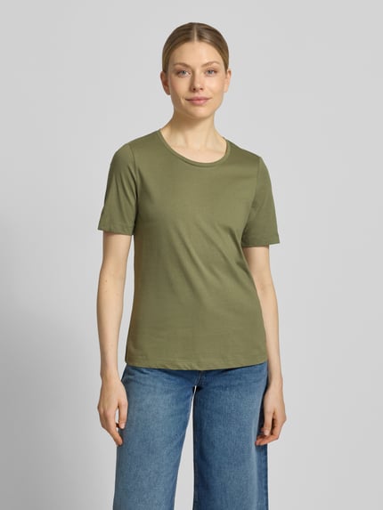 Modelka kobieta nosi T-Shirt mit Rundhalsausschnitt od Christian Berg Woman, czysta bawełna, krój regular fit, półrękaw, długość tyłu w rozmiarze S: 60 cm, oliwkowy, gładka tekstura, pełny widok sylwetki z przodu.