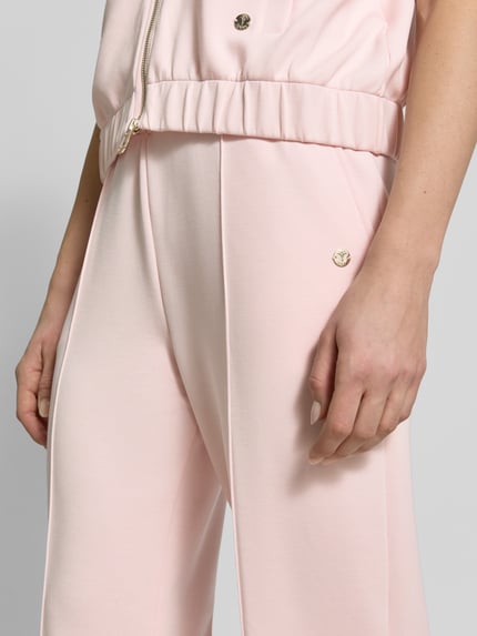 Frauenmodel trägt Sweatpants mit Label-Applikation Modell 'Talila' von JOOP! in zartem Rosa, glatte Struktur, Nahaufnahme Oberschenkel.