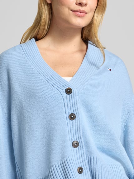 Frauenmodel trägt Cardigan aus Wolle mit Logo-Detail von Tommy Hilfiger in Hellblau, Strickoptik, Knöpfe, Nahaufnahme Oberkörper.