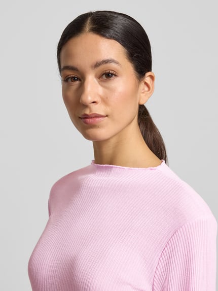 Modelka kobieca nosi Slim Fit Langarmshirt mit Viskose-Anteil od s.Oliver RED LABEL, różowy rippstrick, detal frill, unikolor, krój slim fit, zbliżenie na górną część ciała.