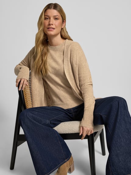 Frauenmodel trägt Strickjacke in offener Passform von Christian Berg Woman aus reiner Baumwolle, beigefarbene Töne, Regular Fit, gerippte Abschlüsse, Rückenlänge 66 cm, Ärmellänge 54 cm, Ganzkörperansicht von vorne.