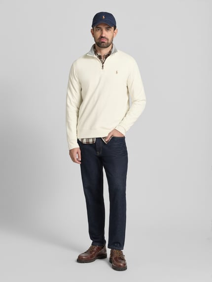 Męski model trägt Bluza mit Label-Stitching von Polo Ralph Lauren z mieszanki bawełny i wiskozy, luźny krój, stójka, krótki zamek błyskawiczny, prążkowane wykończenia, długość tyłu 69 cm, długość rękawów 64 cm, kolor jasny, gładka faktura, Ganzkörperansicht von vorne.