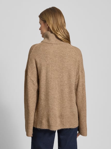 Vrouwenmodel draagt oversized strickpullover met rolkraag van Gina Tricot, beige, geribde boorden, rugaanzicht, materiaal-mix.