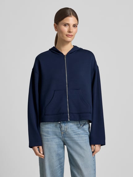Frauenmodel trägt Regular Fit Sweatjacke mit Kapuze von Christian Berg Woman aus Elastischer-Material-Mix mit Modal-Anteil in Dunkelblau, Kängurutasche, Bund mit Tunnelzug, Ganzkörperansicht von vorne.