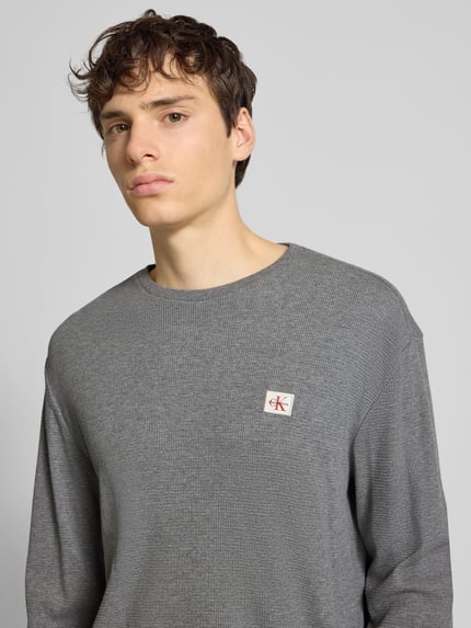 Männermodel trägt graues Slim Fit Longsleeve mit Logo-Patch Modell 'Waffle' von Calvin Klein Jeans, Baumwoll-Mix, Nahaufnahme Oberkörper.