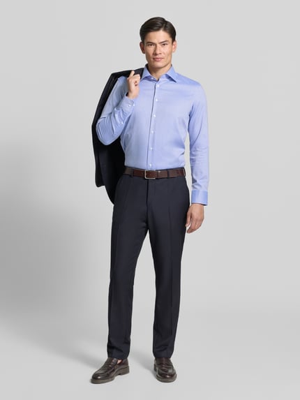 Męski model nosi jasnoniebieską koszulę Slim Fit Businesshemd aus reiner Baumwolle von Seidensticker, spodnie w kolorze granatowym, brązowy pasek, gładka tekstura tkaniny, pełny widok z przodu.