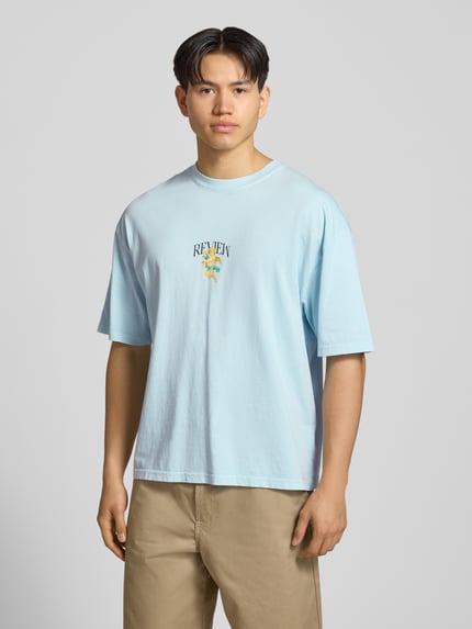 Mannelijk model draagt T-shirt met oversneden schouders van REVIEW in lichtblauw, puur katoen, los model, labelprint, ronde hals, ruglengte maat M 70 cm, vooraanzicht gehele lichaam.