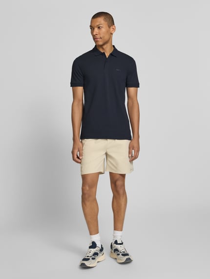 Männermodel trägt Regular Fit Poloshirt aus reiner Baumwolle Modell 'PIO 1' von BOSS Green, unifarben, kurze Knopfleiste, Ganzkörperansicht von vorne.