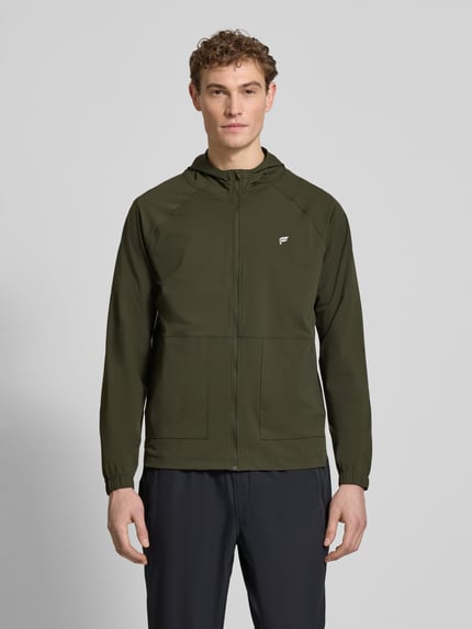 Męski model nosi Regular Fit Jacke mit Kapuze Modell 'The One' von Fabletics z elastycznej mieszanki materiałów, krój regular fit, kaptur, zamek błyskawiczny, nakładane kieszenie, nadruk z logo, długość tyłu w rozmiarze M: 71 cm, szerokość ramion w rozmiarze M: 44 cm, szerokość klatki piersiowej w rozmiarze M: 34 cm, długość rękawów w rozmiarze M: 68 cm, ciemnozielony kolor; Ganzkörperansicht von vorne.