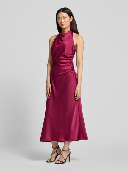 Frauenmodel trägt Knielanges Cocktailkleid aus Satin von Hey Kyla in dunklem Rot, Ärmelloses-Design, Körpernahe Passform mit Raffungen, Ganzkörperansicht von vorne, Elastischer-Material-Mix, Satin, Rückenlänge 97 cm, Brustweite 38 cm.