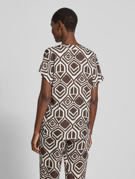 Frauenmodel trägt Regular Fit Bluse aus Viskose Modell 'Amber' von TONI im Allover-Look mit V-Ausschnitt, Rückenlänge 63 cm, Ärmellänge 15 cm, Geometrie-Muster in Braun und Weiß, Ganzkörperansicht Rückansicht.