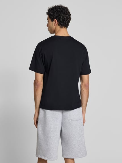 Männermodel trägt T-Shirt mit Logo und Rundhalsausschnitt von REVIEW, schwarze Reine Baumwolle, Relaxed-Fit, Rückenlänge 68 cm, Ganzkörperansicht Rückansicht.